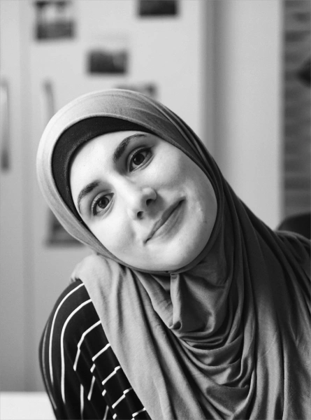 Photo de Sara Soueidan en noir et blanc. Elle a la tête penchée sur le côté et nous sourit. Elle a l'air très fière de ce qu'elle a créé.