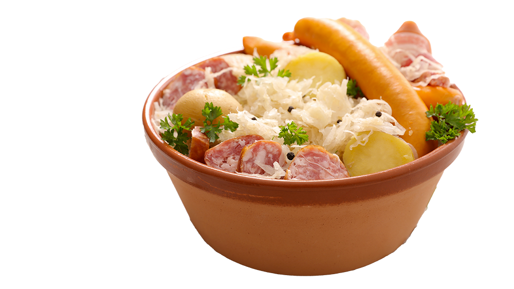 Une choucroute dans un bol en terre cuite, avec des pommes de terre, deux morceaux de saucisse, du saucisson et des feuilles de coriandre